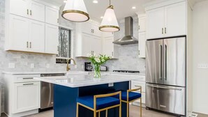 Una cocina moderna con armarios blancos, un refrigerador de acero inoxidable y un taburete azul.
