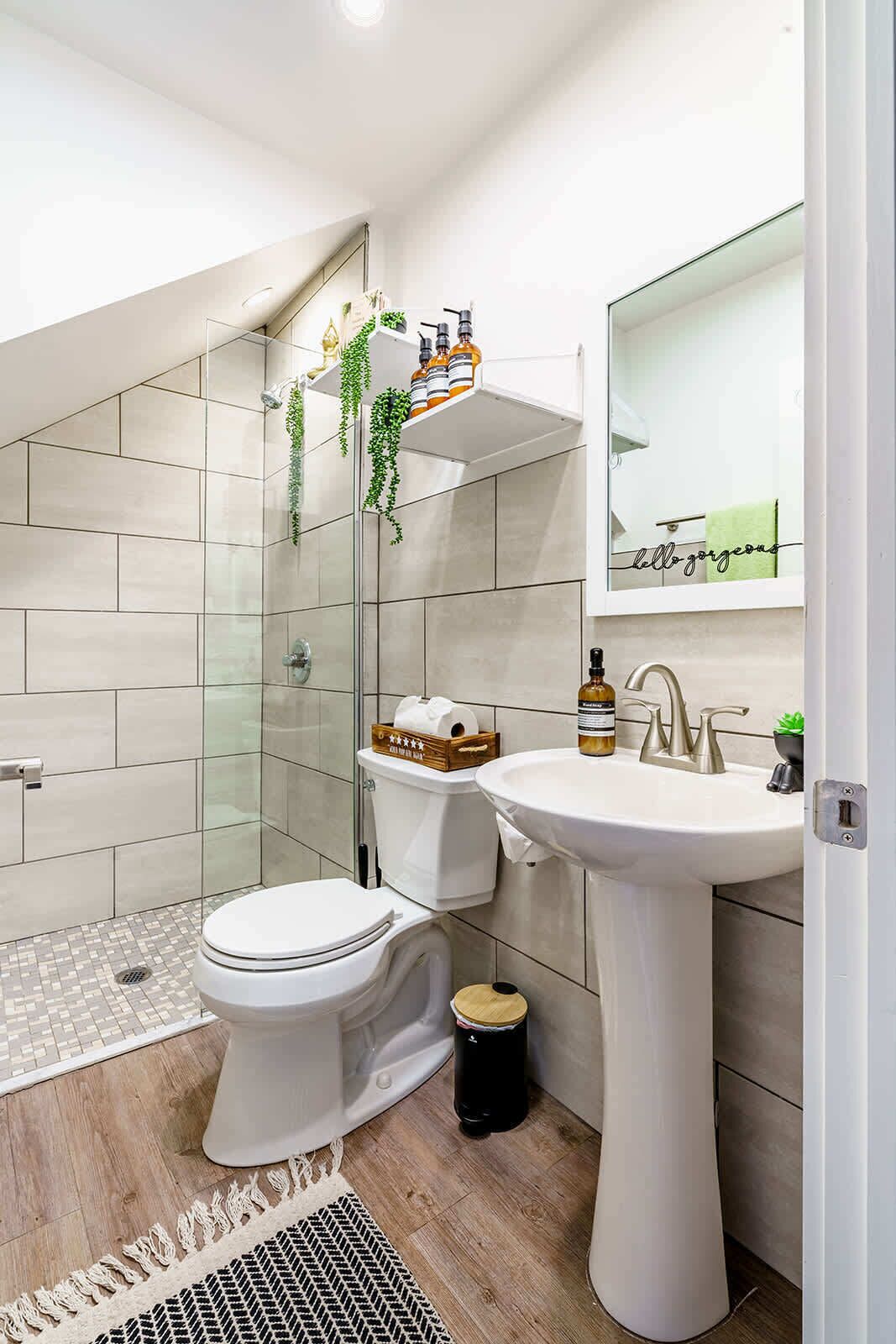 Un baño moderno con cabina de ducha de vidrio, inodoro blanco, lavamanos pedestal y espejo con marco decorativo.