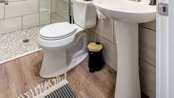Un baño moderno con cabina de ducha de vidrio, inodoro blanco, lavamanos pedestal y espejo con marco decorativo.