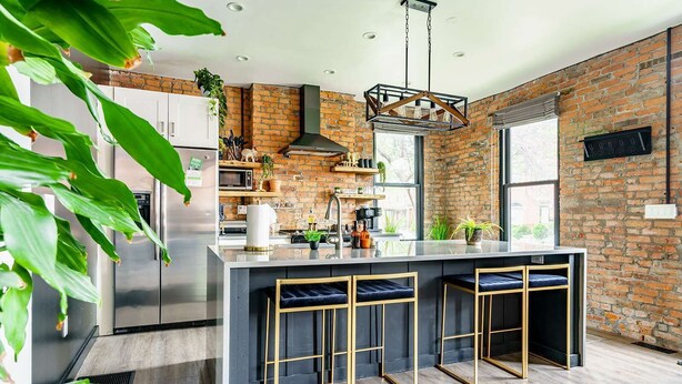 Una cocina moderna con una isla central, taburetes de bar, una lámpara colgante y una pared de ladrillo.