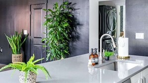 Una cocina moderna con encimera blanca, lavavajillas integrado y una gran planta en maceta.
