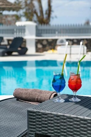 A poolside setting with two drinks in glasses, a towel, and lounge chairs. - Black Coast Hotel Santorini (Santorini)