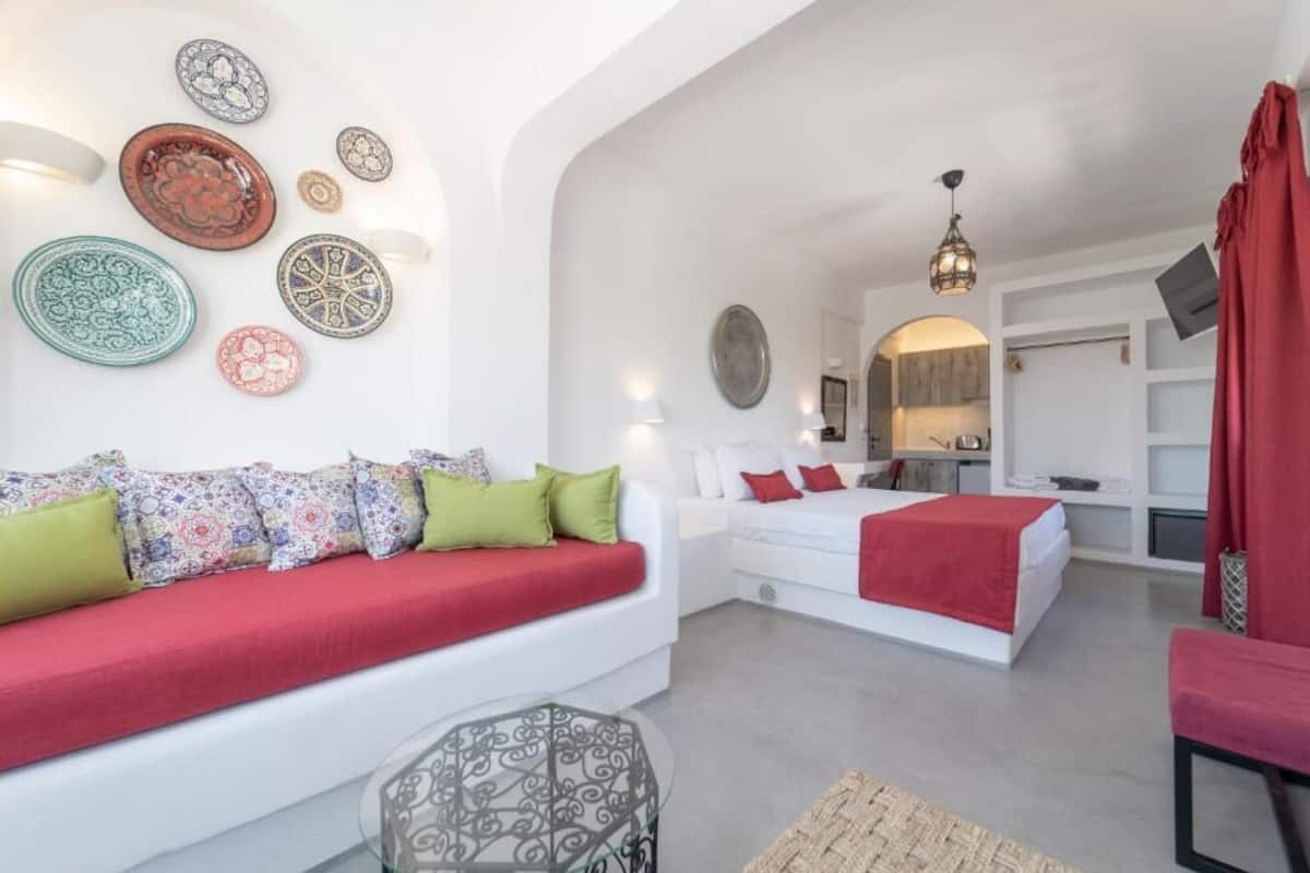 A modern bedroom with a red sofa, a white bed, and a dining area with a red curtain.