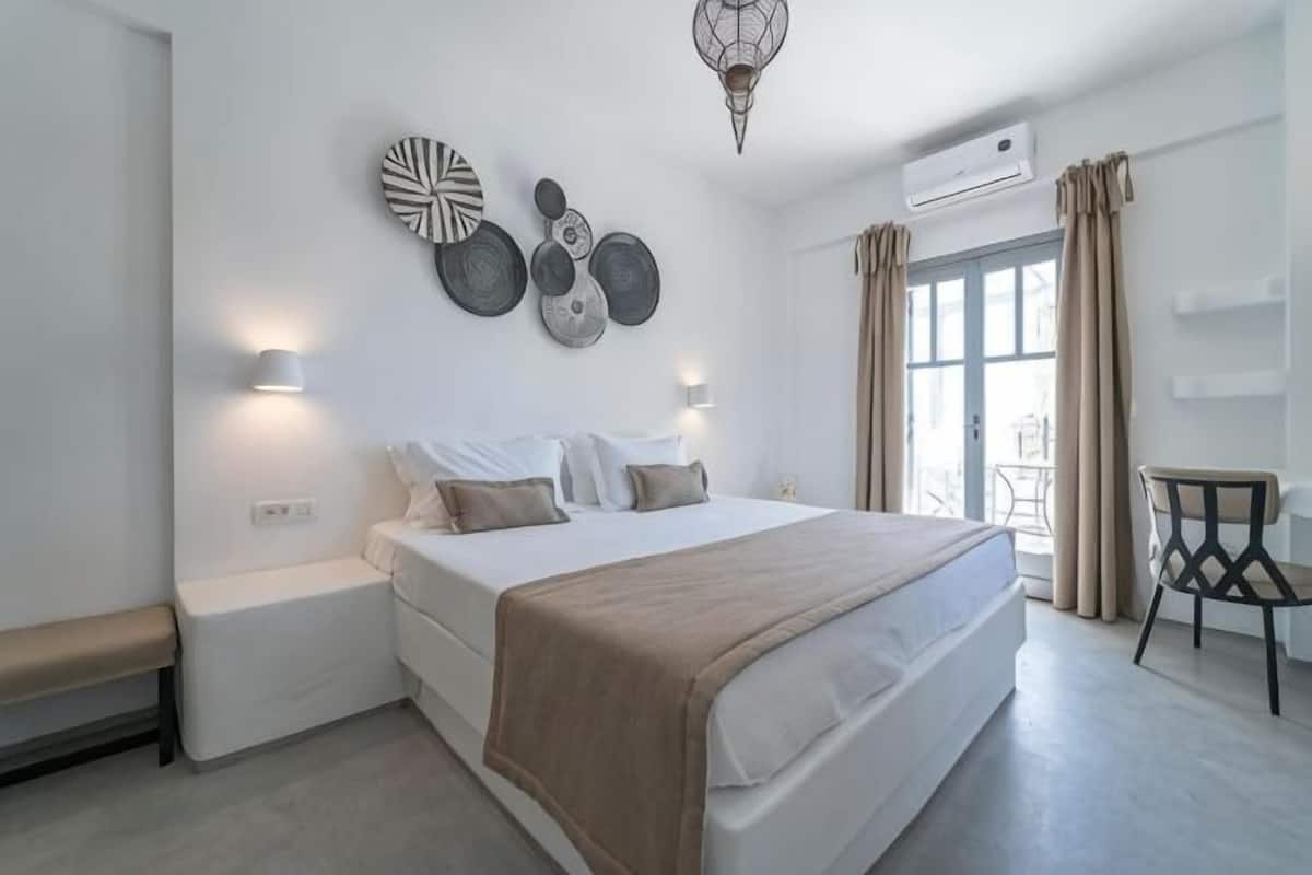 A bedroom with a bed, bedside tables, wall art, and a view through the window.