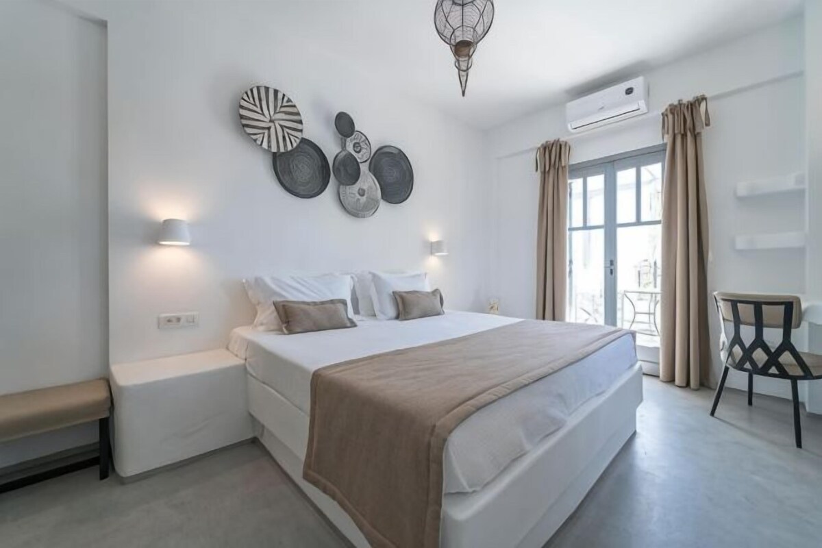 Une chambre à coucher avec un lit, des tables de chevet, des œuvres d’art murales et une vue par la fenêtre.