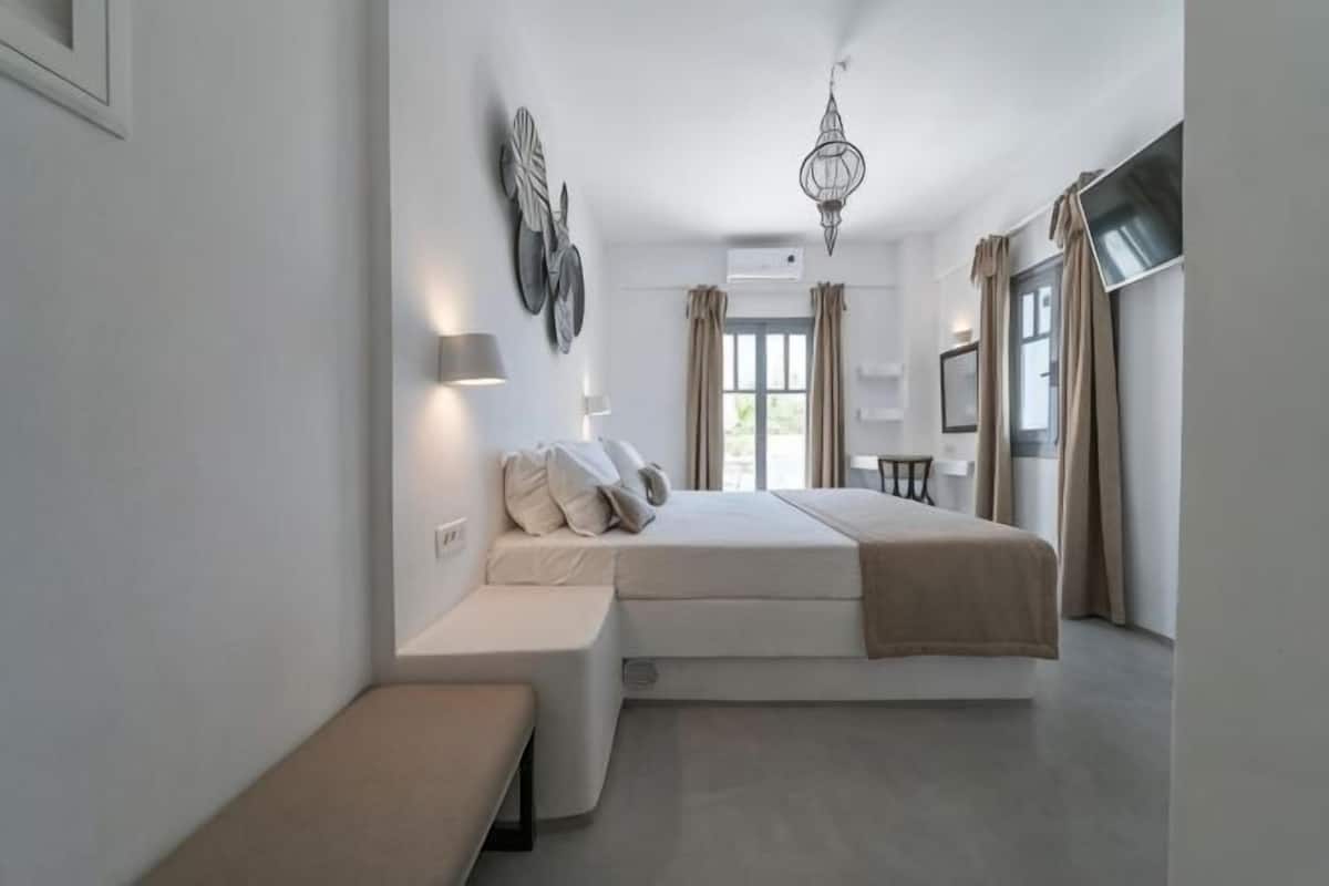 A modern bedroom with a large bed, bedside tables, a bench, and a chandelier.