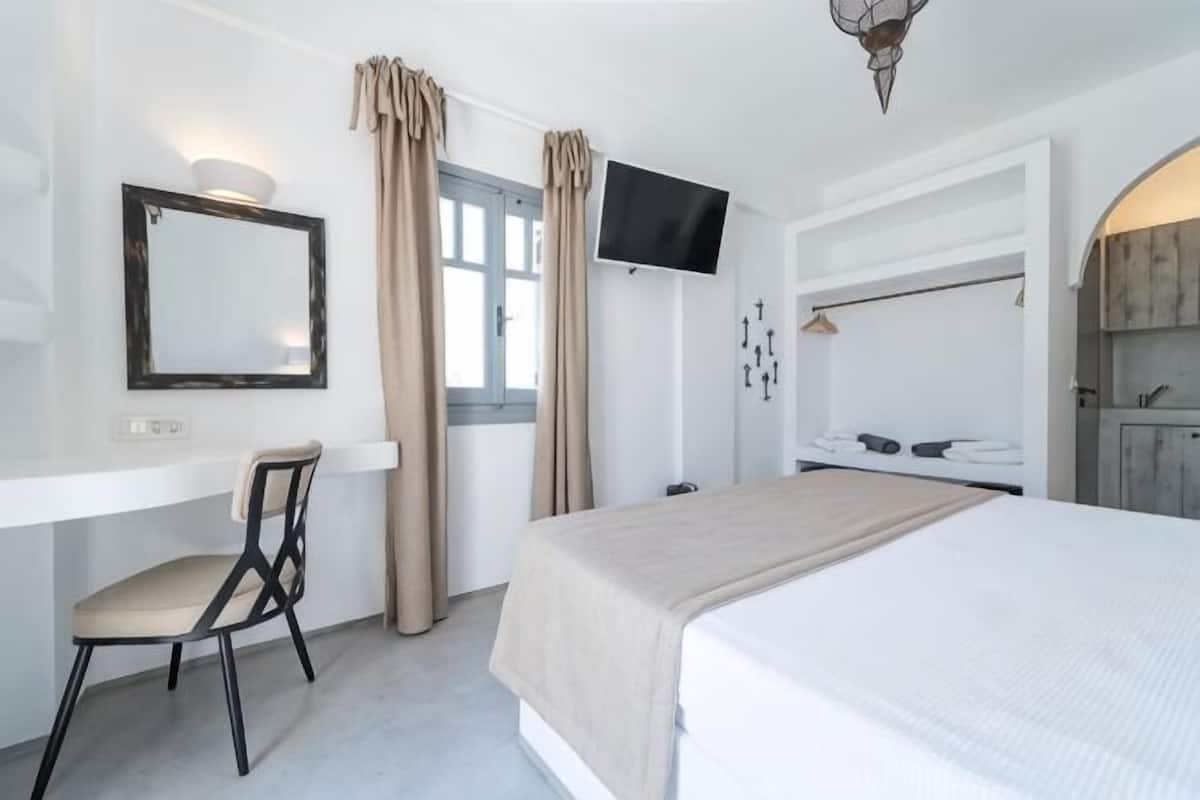 A hotel room with a bed, a desk with a chair, a television, and a window with curtains.