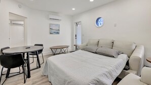 A bedroom with a bed, a round table, a chair, a small table, and an air conditioning unit. - Banyan St 2BR/1BA off Las Olas- Steps to Beach #1 (Fort Lauderdale)