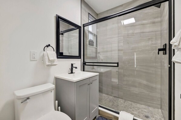 A modern bathroom with a toilet, sink, and glass shower enclosure.