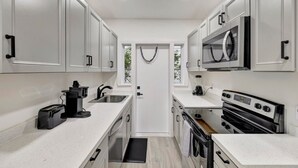 Une cuisine moderne avec des armoires blanches, un four à micro-ondes encastré, une cuisinière et un évier.