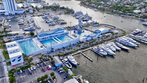 Une vue aérienne d’une marina où sont amarrés de nombreux bateaux, avec une piscine et un espace de stationnement.