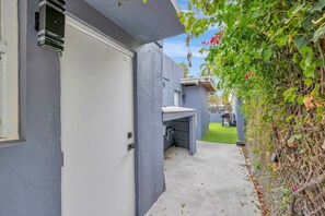 Une ruelle étroite avec une porte grise, un petit banc en béton et une pelouse verte en arrière-plan.