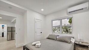 Ein Schlafzimmer mit einem Bett, einem Nachttisch, einem Fenster und einer Klimaanlage.