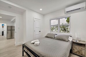 Een slaapkamer met een bed, nachtkastje, raam en een airconditioning.