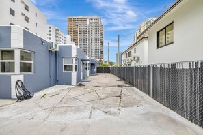 A narrow alleyway between buildings with a chain-link fence on one side and a building with a white facade on the other.