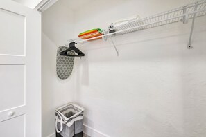 A laundry area with a drying rack, a hanging rack, and a trash bin.