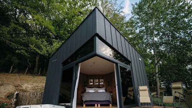 A modern, dark-colored cabin with a large glass door leading to a bedroom with a bed and two chairs. - PurpleVague (Runcu)
