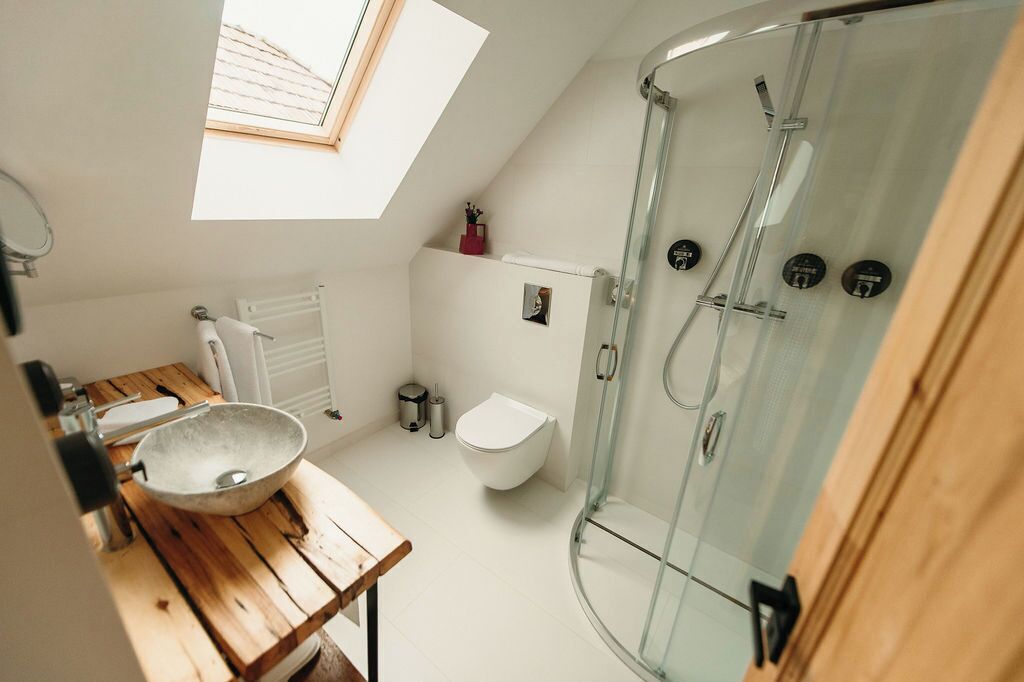 A modern bathroom with a skylight, a wooden vanity, a glass shower enclosure, and a white toilet.
