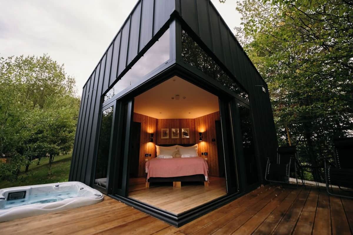 Un dormitorio acogedor y moderno con piso de madera, una cama grande y un jacuzzi afuera.