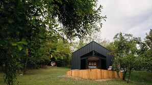 A modern, dark-colored cabin with a wooden deck, surrounded by lush greenery and trees. - PurpleVague (Runcu)