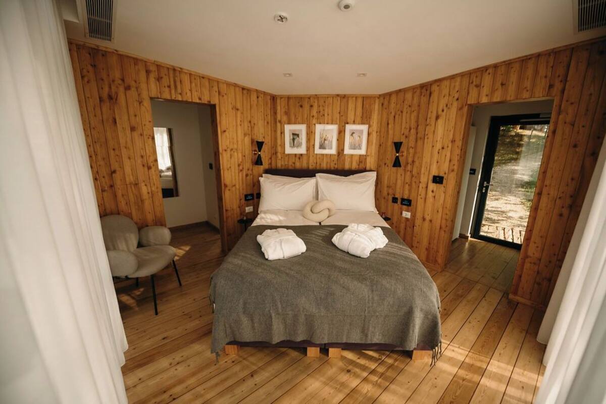 Un dormitorio con un muro revestido de madera, una cama con ropa de cama blanca, una silla y una puerta que da al exterior.