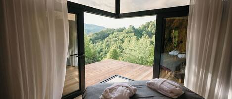 A bedroom with a large window offering a view of a forested area.
