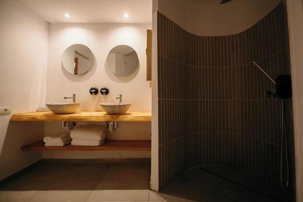 Een badkamer met twee ronde spiegels, een houten aanrecht en een douche met verticale lijnen.