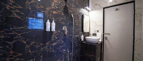 Un baño moderno con pared de mármol negro, lavamanos blanco y ducha.