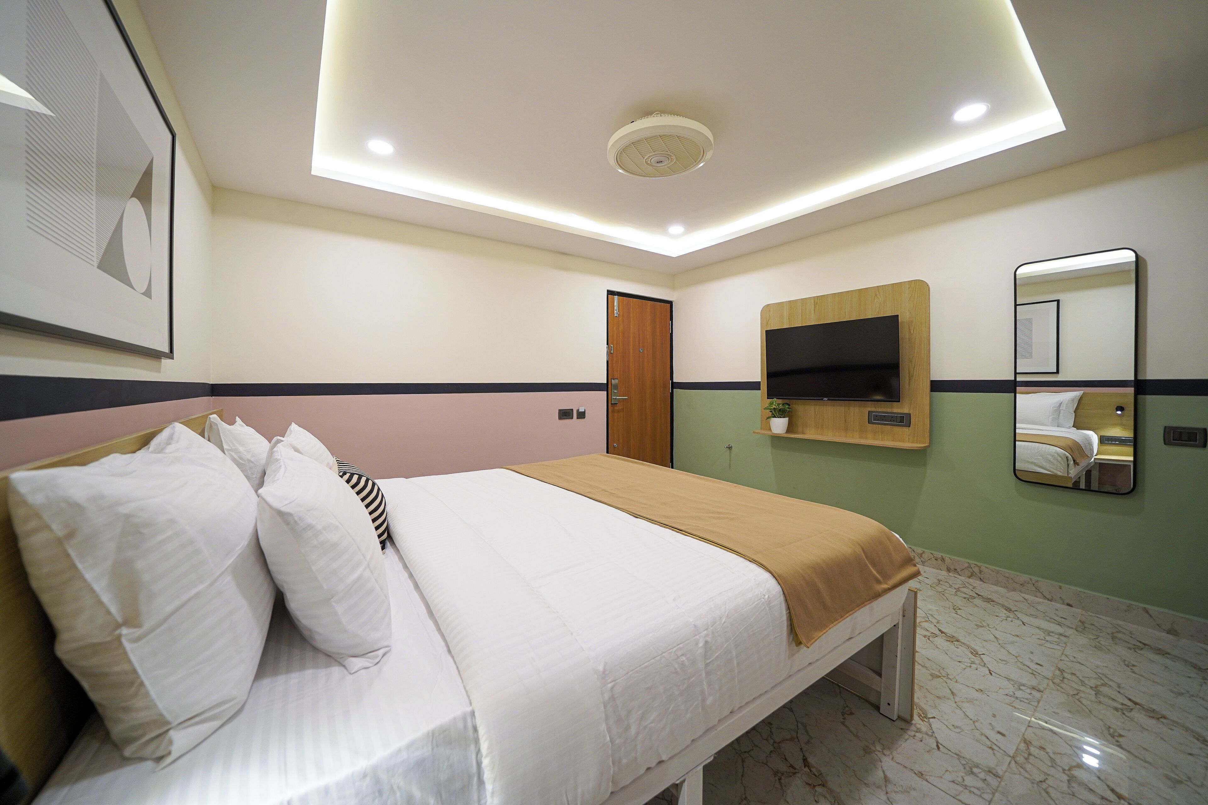 A hotel room with a bed, a TV mounted on the wall, a mirror, and a door.