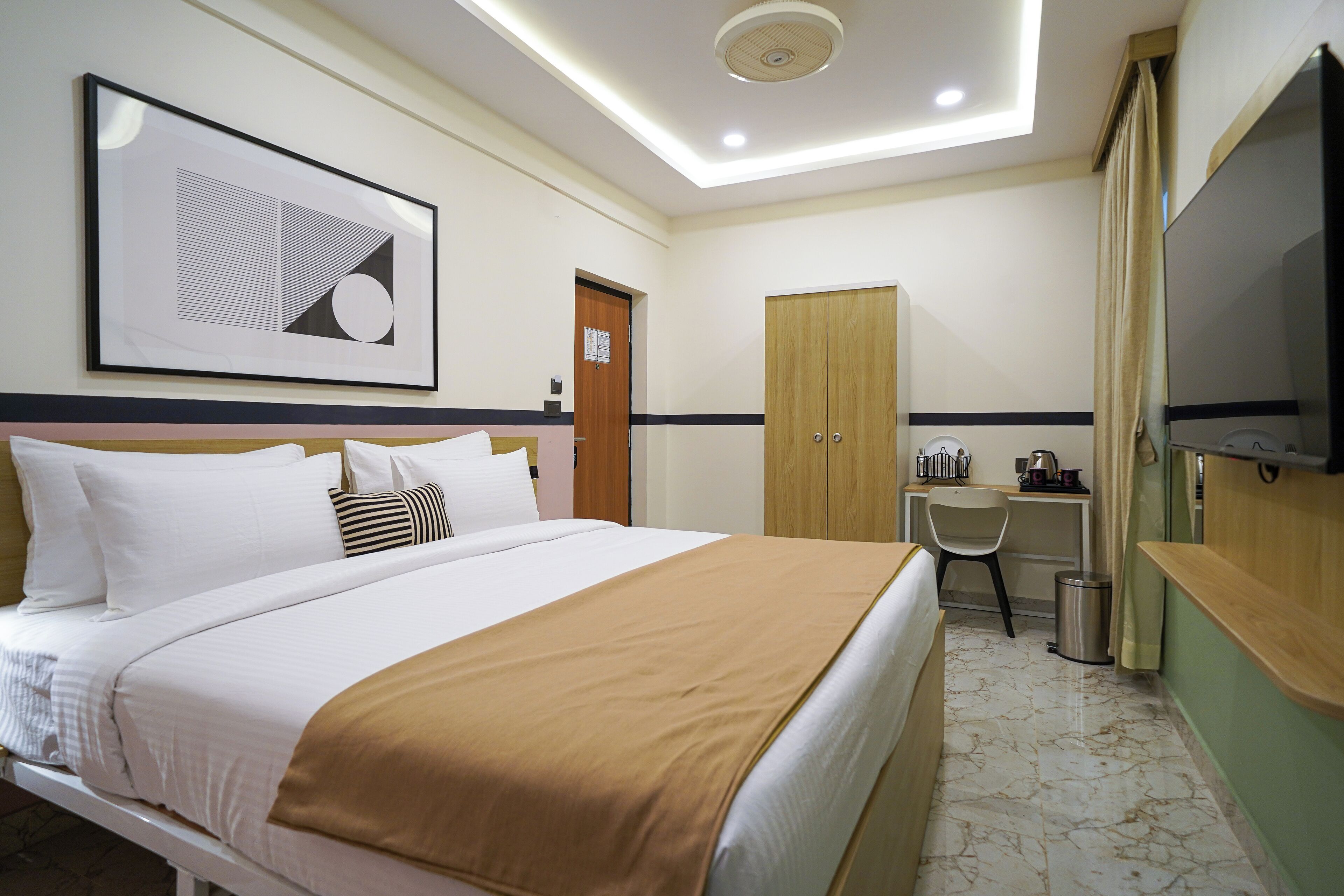 A hotel room with a bed, a desk, a chair, a television, and a framed picture on the wall.