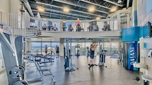 A gym with weightlifting equipment, a mezzanine level with a railing, and a view of the outside.
