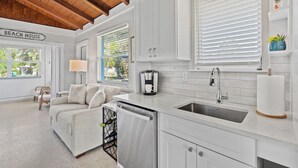 A modern kitchen with white cabinetry, a dishwasher, and a sink. There is a sign that reads "BEACH HOUSE" on the wall. - Charming Naples Retreat – Your Perfect Getaway! (Naples)