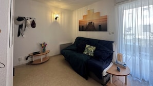 Una habitación acogedora con un sofá verde oscuro, una mesita de madera, una lámpara de pared y un ventilador de techo.