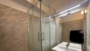 Un baño moderno con ducha de vidrio, lavabo blanco y espejo.