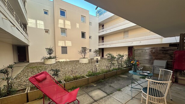 Un patio con una silla roja plegable, una mesa con sillas y plantas en macetas.