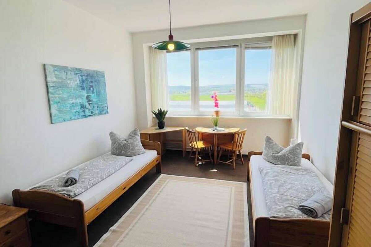 Une chambre de taille modeste, comprenant deux lits simples, une petite table et une chaise.