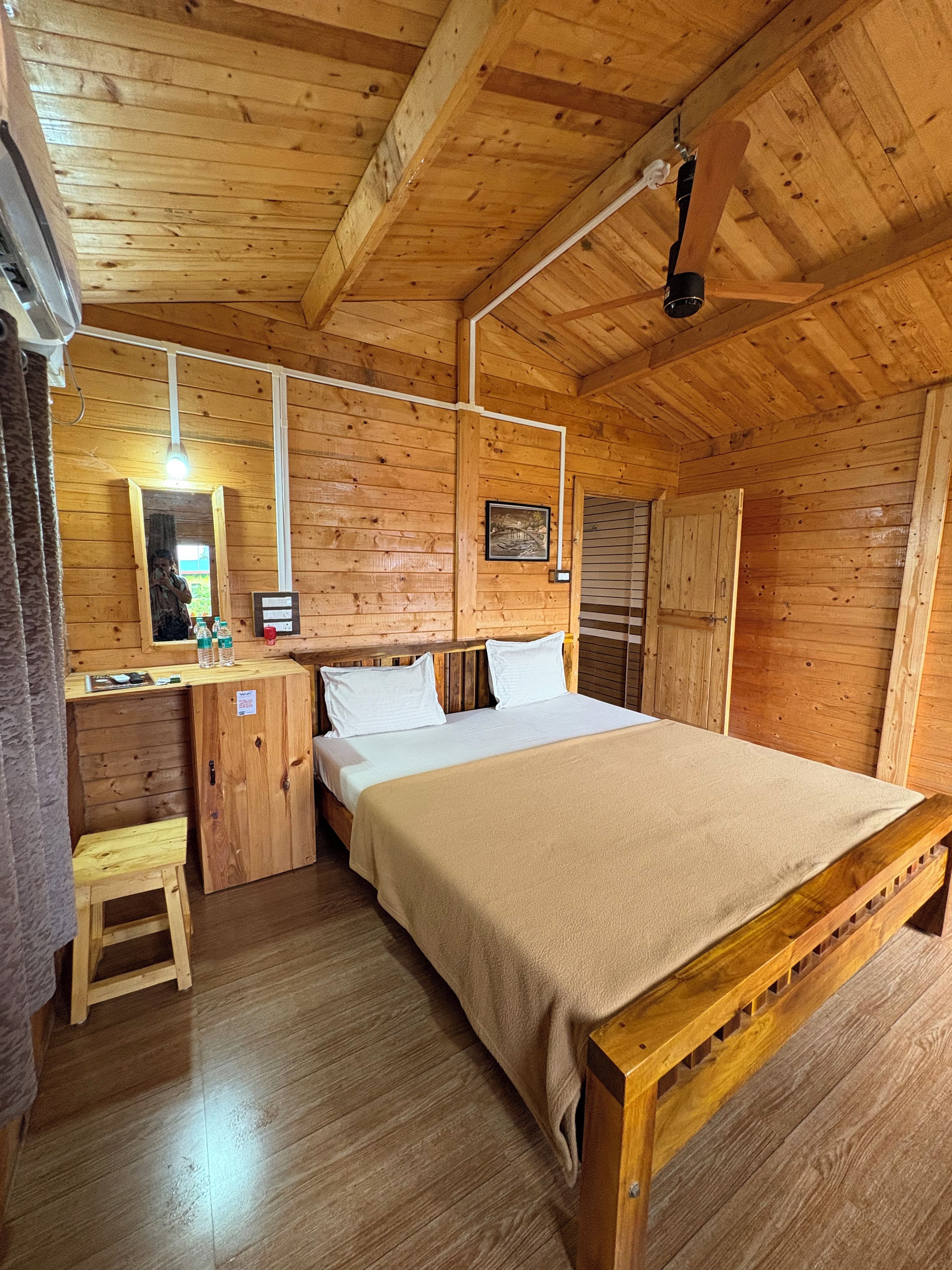 Een houten kamer met een bed, een bureau, een spiegel en een plafondventilator.
