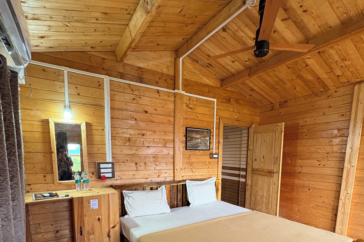 A wooden cabin room with a bed, a small desk, a mirror, and a ceiling fan.