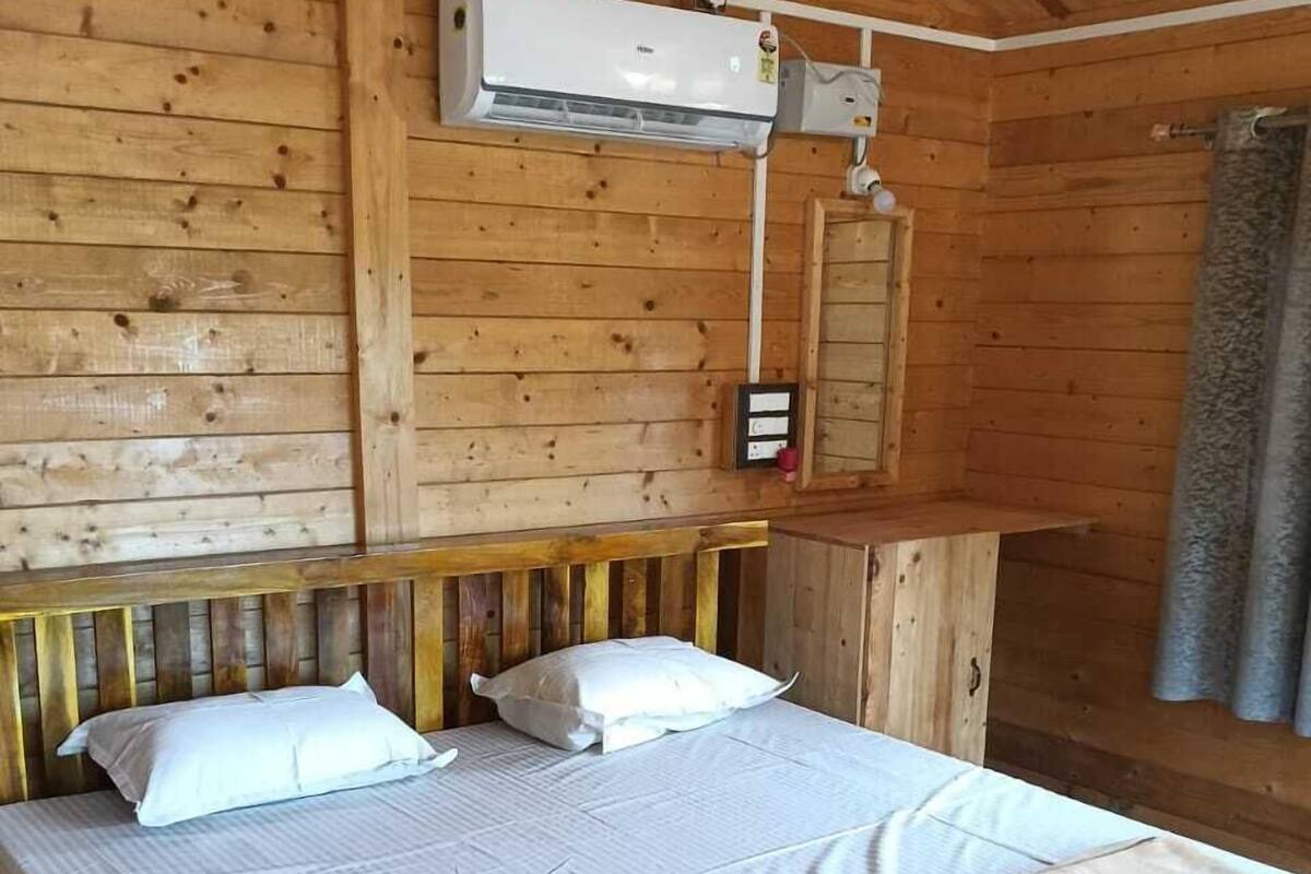 Habitació de cabana de fusta amb llit, almoades, una manta, un aparell d'aire condicionat i una taula de fusta petita.