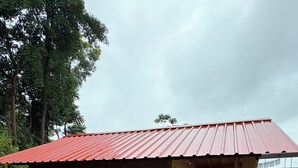 Una cabaña de madera con techo rojo, un porche con cerca de madera y un jardín con diversas plantas.