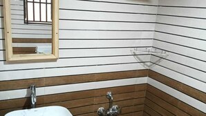 Un bagno con un lavandino bianco, rivestimento in legno, uno specchio, una doccia e un secchio verde.