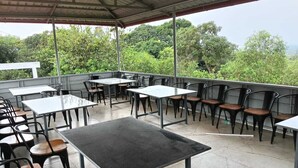 Zona patio esterna con tavoli e sedie, circondata dal verde.