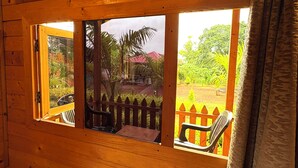 Una cabaña de madera con ventanal a un jardín y un edificio de techo rojo.