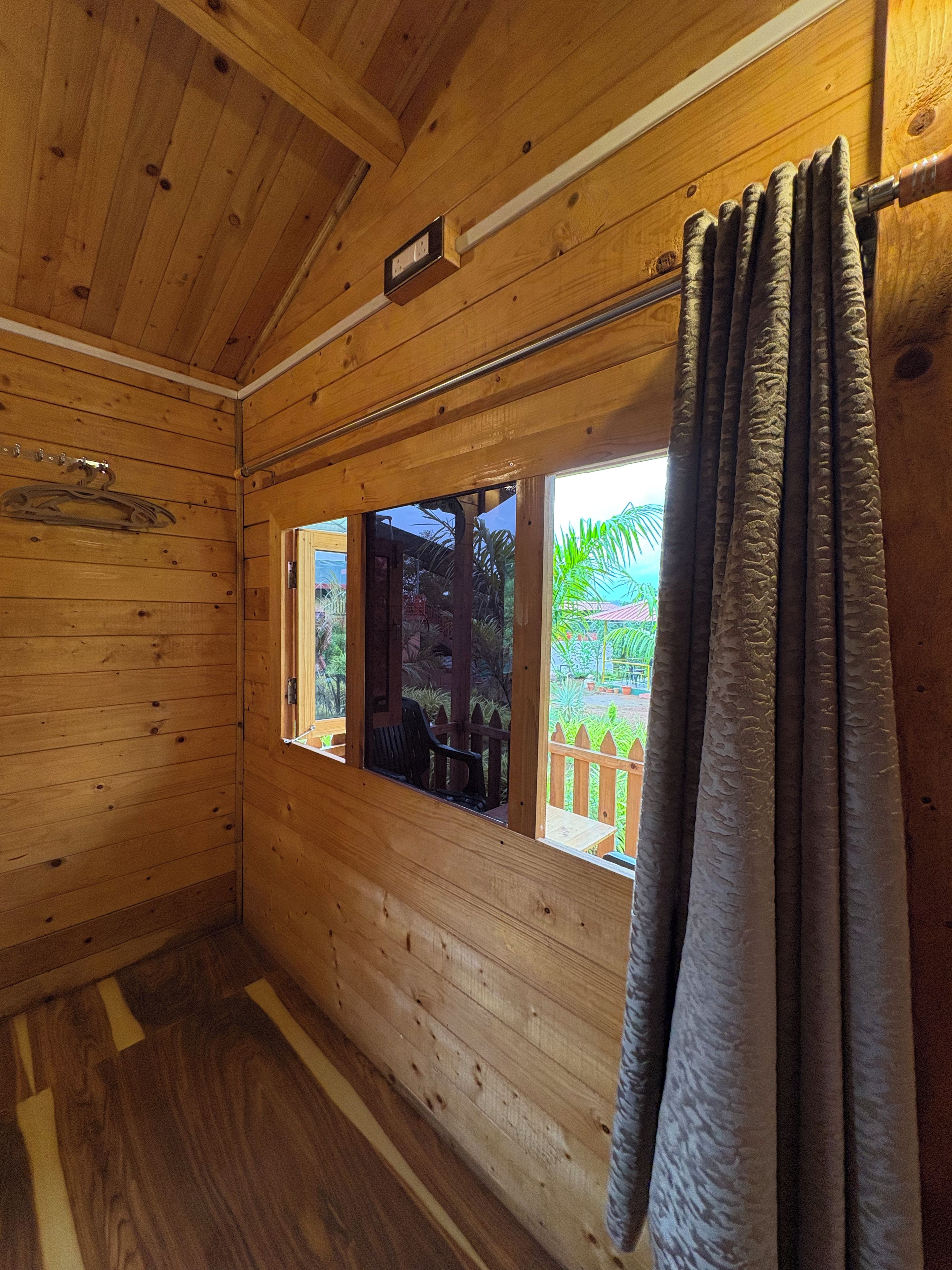 Una habitación de cabaña de madera con ventana, cortina y suelo de madera.
