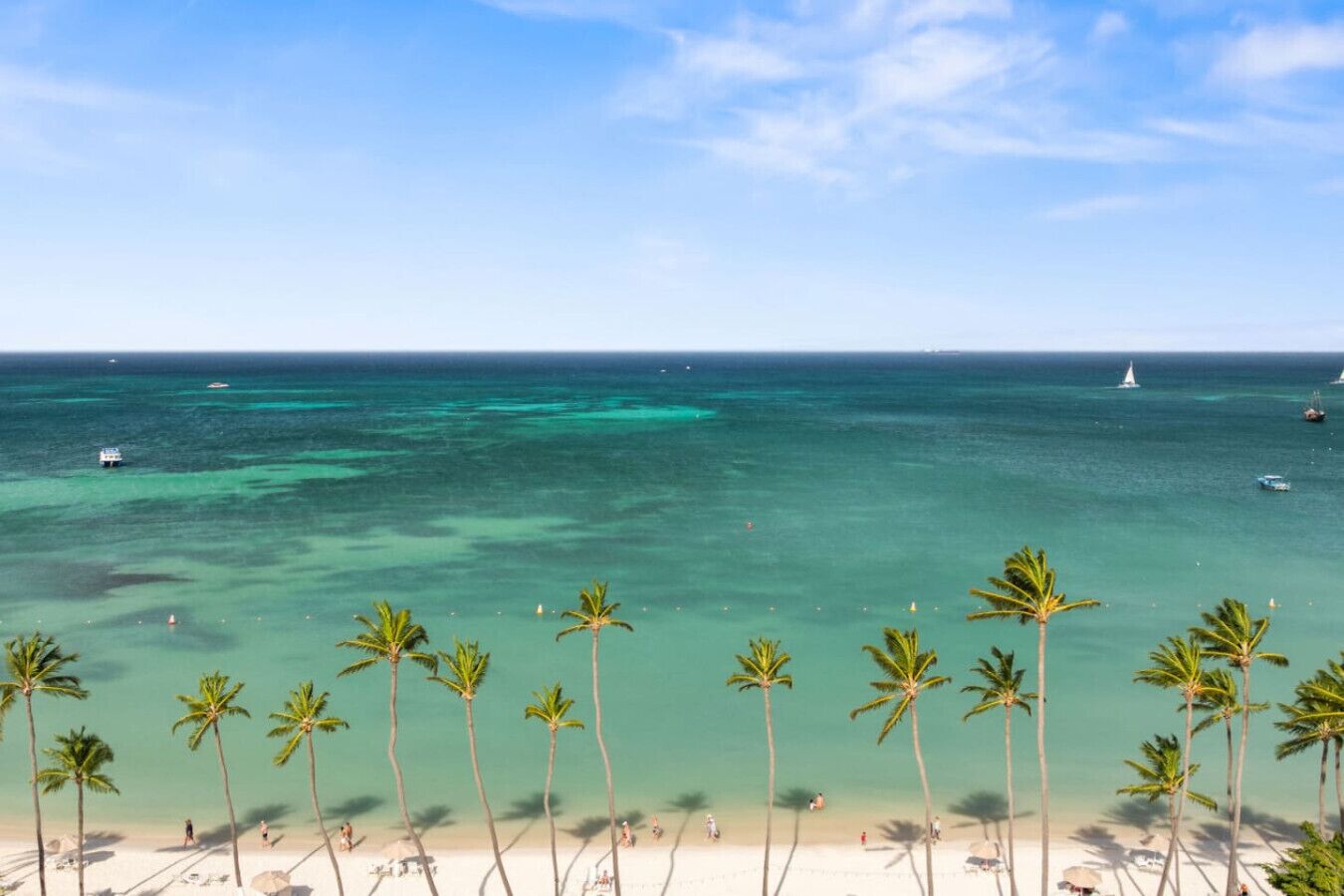 A beach with clear turquoise water, palm trees, and a boat in the distance.
