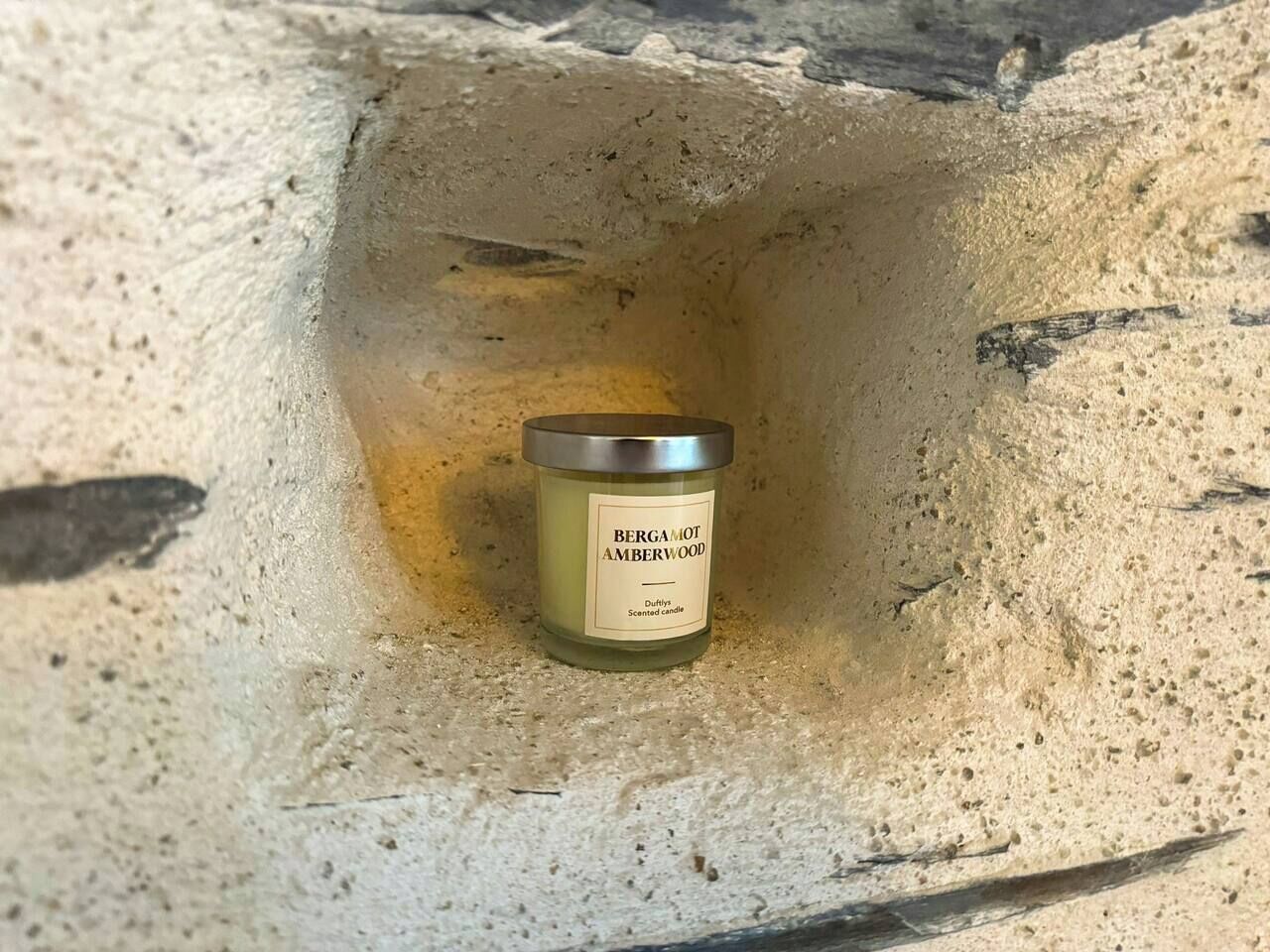 A candle labeled 'BERGAMOT AMBERWOOD' in a stone crevice.