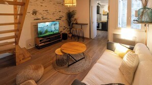 A modern living room with a wooden staircase, a TV, a round coffee table, and a sofa. - Charming Bright Duplex (Angers)