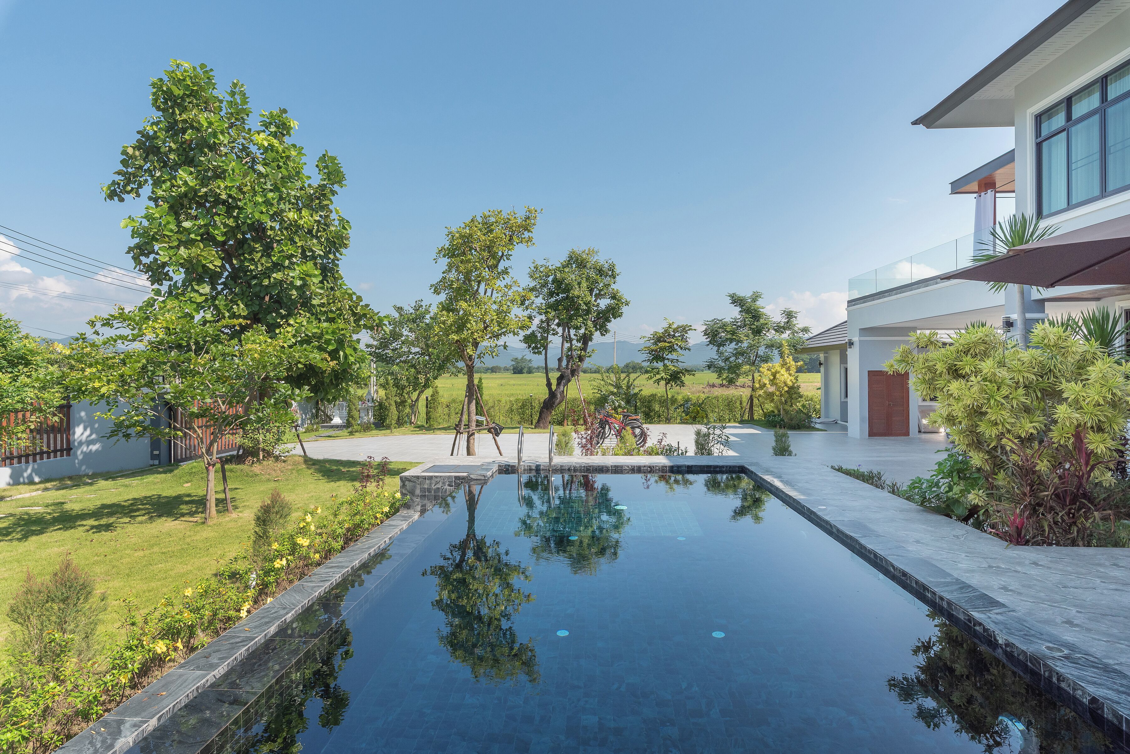 A modern house with a swimming pool, surrounded by greenery and a clear sky.