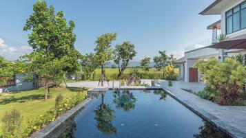 A modern house with a swimming pool, surrounded by greenery and a clear sky.