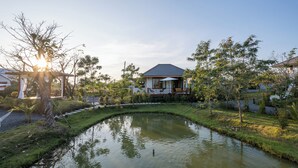 A serene pond with a small water feature in the center, surrounded by well-maintained grass and trees.